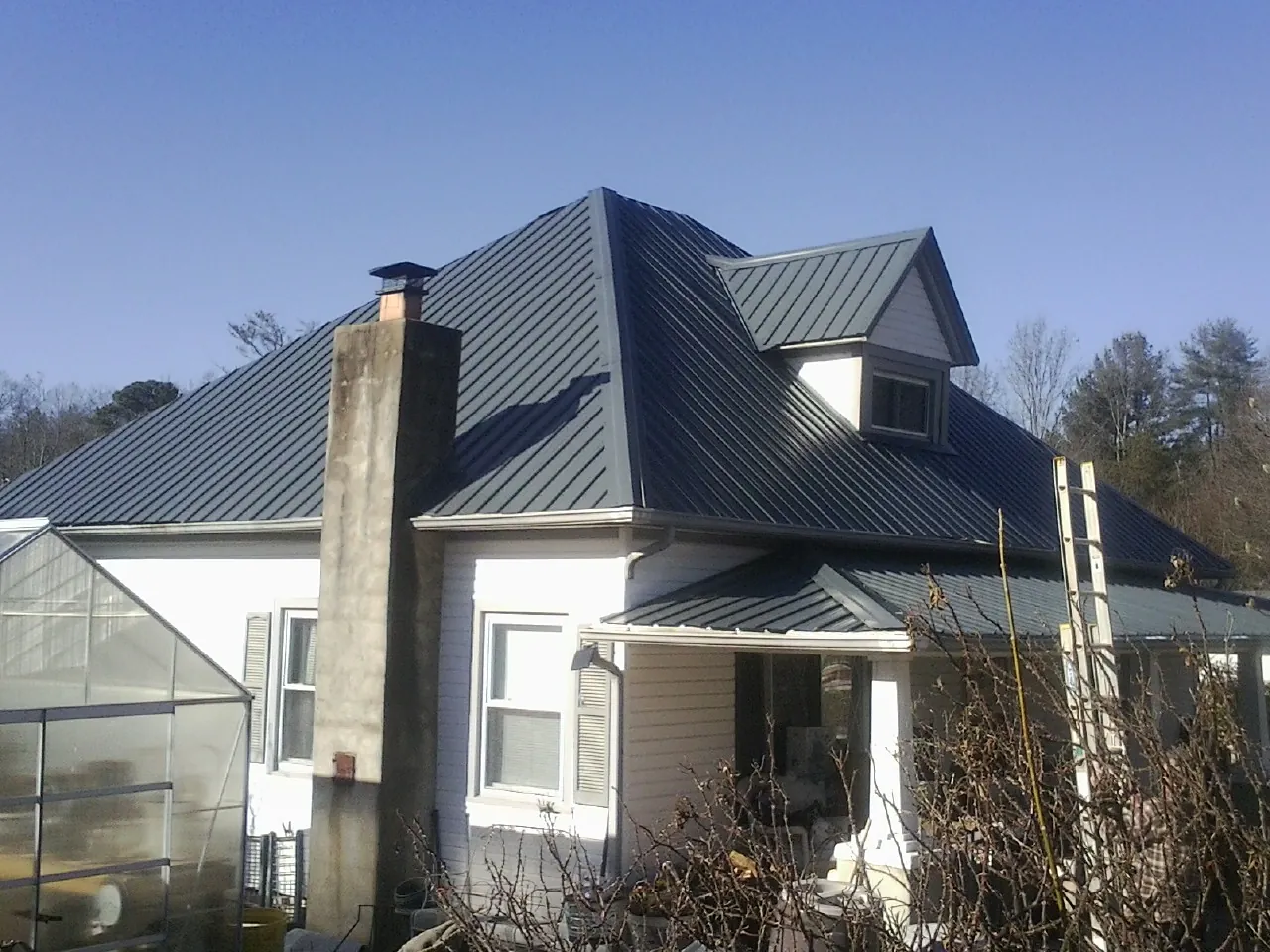 Dark blue standing seam metal roof on a white farmhouse with dormer — Slate & Tile Roof Repair by Roofing Brothers in Shingletown