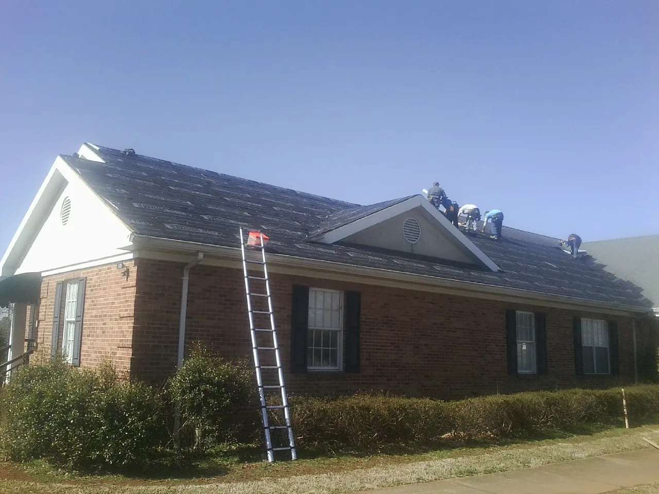 Crew tearing shingles off a brick ranch roof with a ladder set — Metal Roof Repair work by our crew in Shingletown