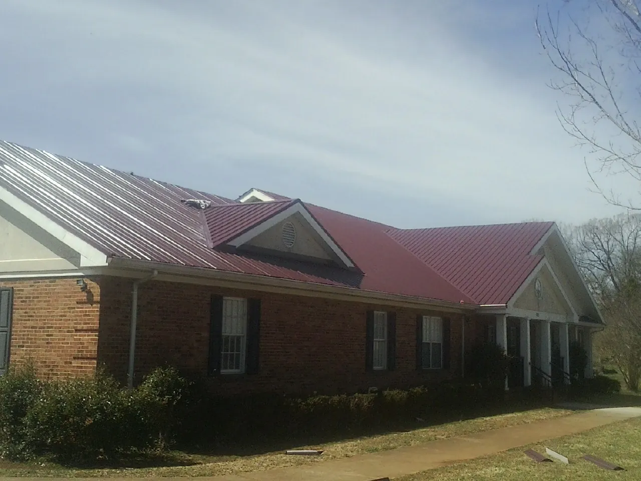 Red metal roof with gabled entries on a long brick building, from a Hail Damage Roof Repair job in Shingletown